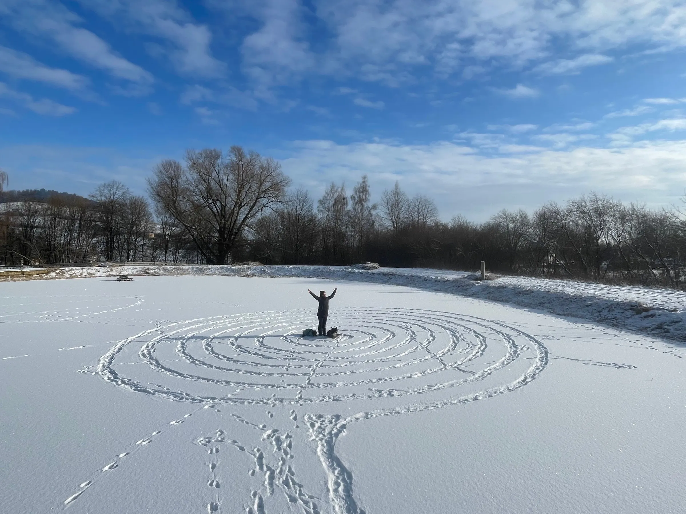 Eine große Spirale im Schnee, in der Mitte steht ein Mensch mit erhobenen Armen